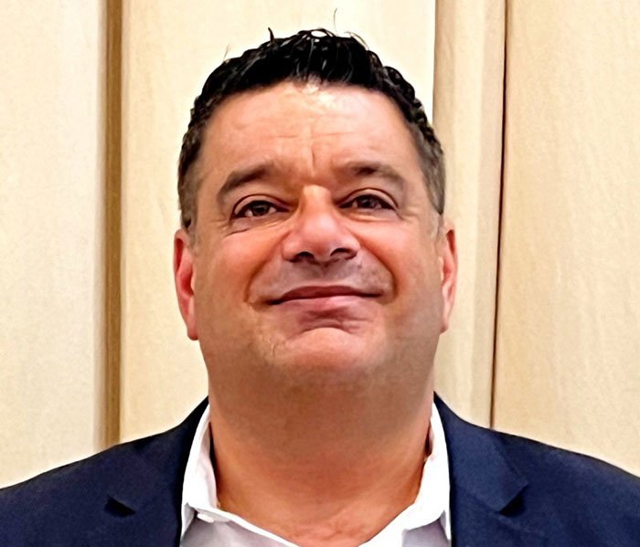 Middle-aged man in a dark suit smiling against a beige background related to Campbell's executive leaked audio on soup ingredients.