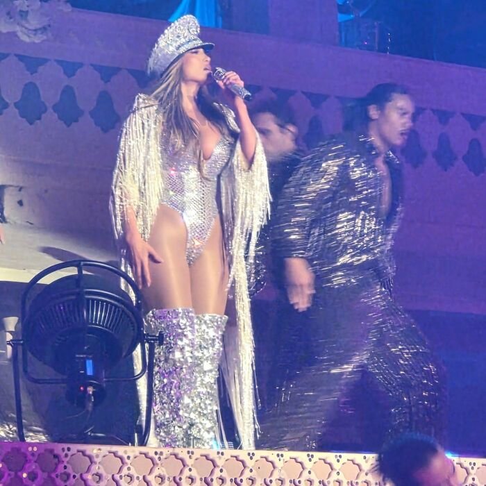 Jennifer Lopez in a sparkling outfit performing on stage at a billionaire wedding during a risqué show.