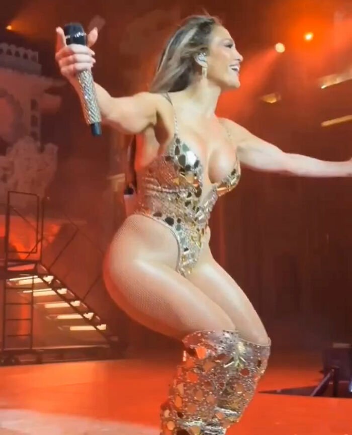 Jennifer Lopez performing in a risqué gold outfit on stage during a billionaire's wedding event with dramatic lighting.