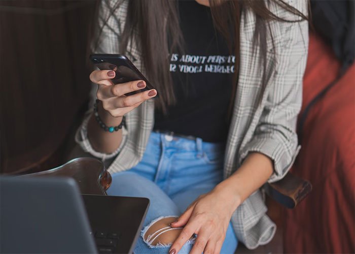 Woman sitting with phone and laptop, reacting to texts revealing friends’ negative feelings about birthday parties.