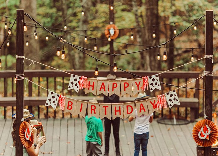 Outdoor birthday party decorations with happy birthday banner and children playing on a wooden deck in autumn.