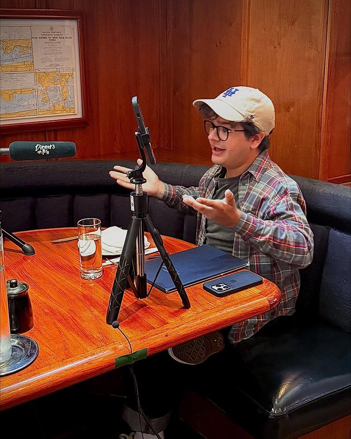 Stranger Things actor Gaten Matarazzo speaking during a casual interview setup at a wooden table with recording equipment.