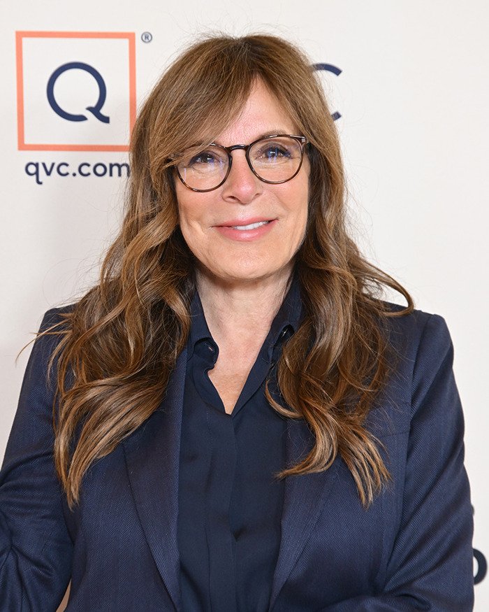 Woman with long brown hair and glasses in a navy blazer, smiling at an event featuring Meghan Markle royal gesture news.