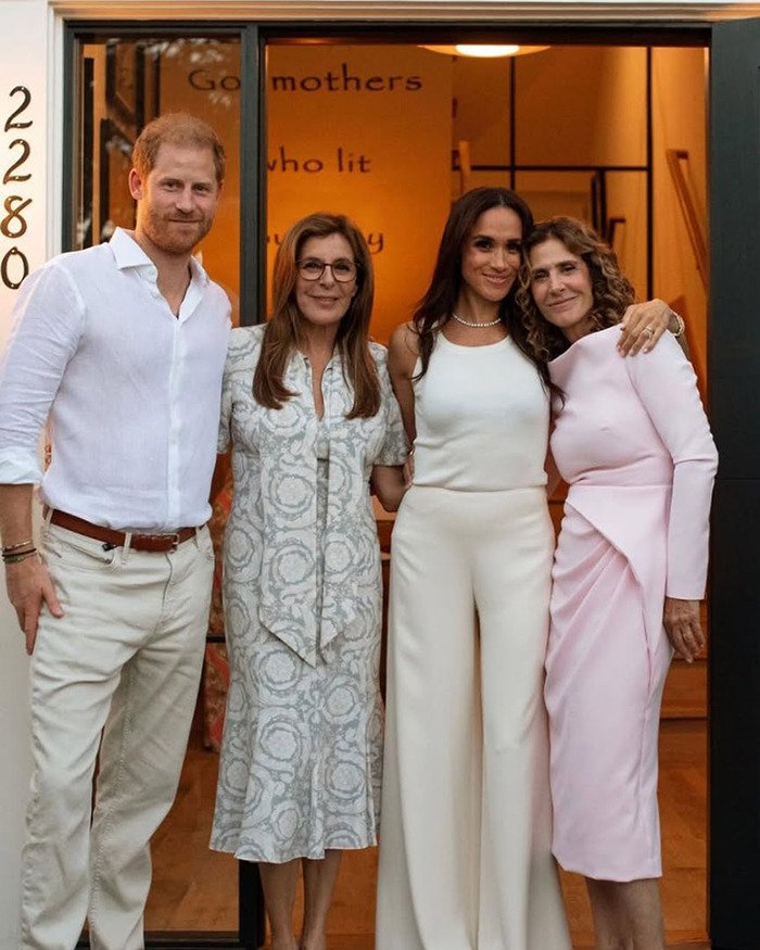 Meghan Markle standing with three people in casual attire inside a warmly lit room during a social event.