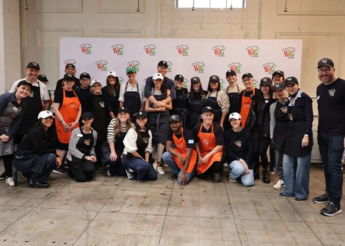 Group of volunteers wearing aprons and caps posing indoors at a charity event related to Meghan Markle royal gesture controversy.