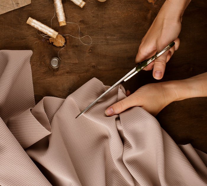 Hands cutting fabric with scissors on a wooden table, sewing supplies nearby, illustrating dress alteration without permission.