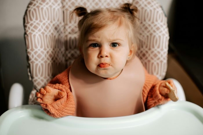 Toddler girl in a high chair looking upset, illustrating mom's concern about how her kids act and behave.