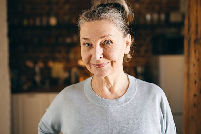 Older woman smiling slightly, representing mother revealing true colors in texts, causing ties to be cut with son.