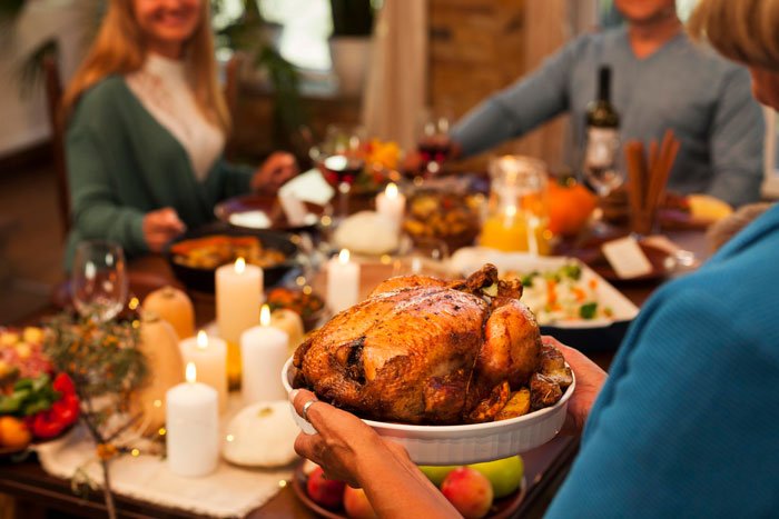 Family gathered around Thanksgiving table with roasted turkey, highlighting husband’s pressure buying Thanksgiving items.