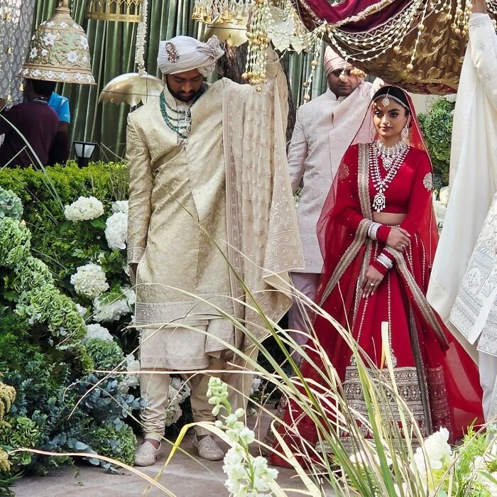 Bride and groom in traditional attire at a lavish wedding, with floral decor and intricate fabric details.