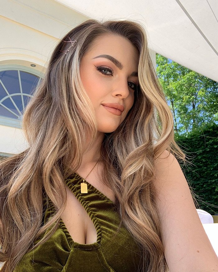 Influencer with long wavy hair and makeup posing outdoors, hinting at mystery surrounding her vanishing after Christmas party.