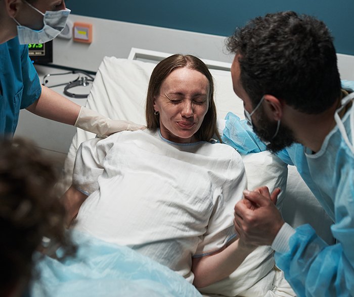 Pregnant woman in hospital bed supported by partner and medical staff during birth support experience.