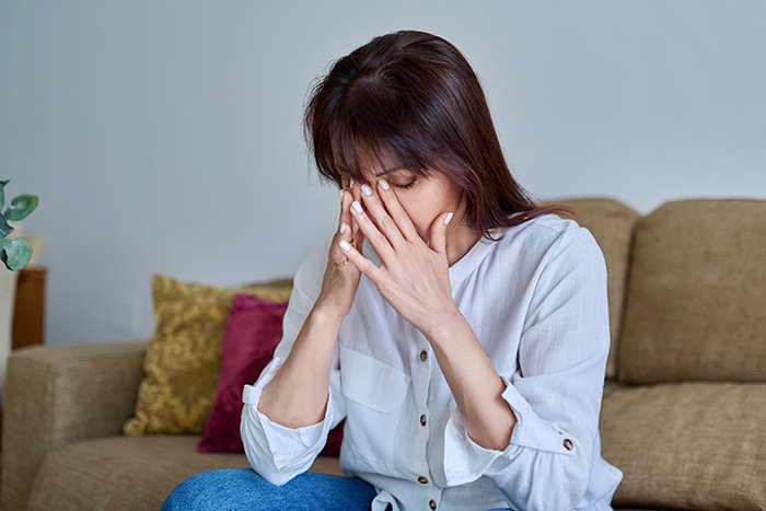 Woman sitting on couch, distressed and covering her face, reflecting on inspiring 5 year update after leaving cheating husband.