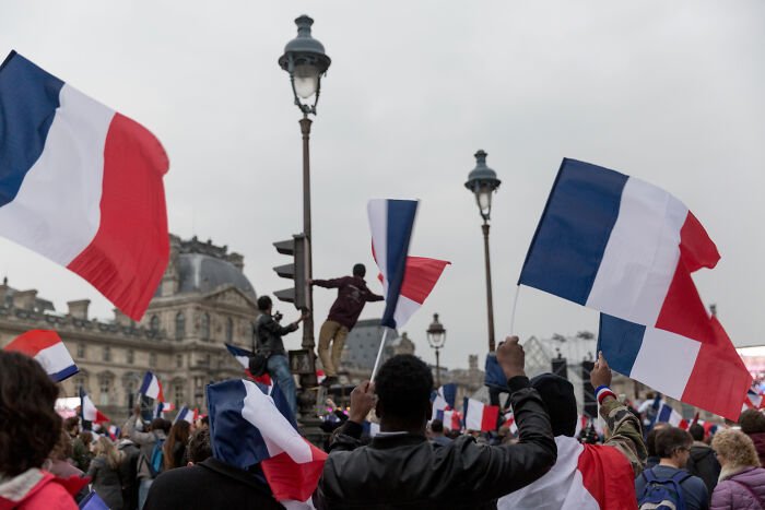 Crowd waving French flags during protest as France is boiling amid soldiers' odd behavior and political tensions.