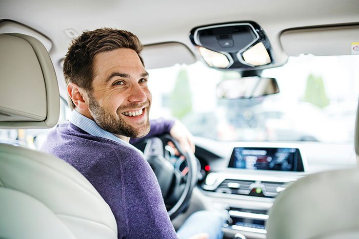 Smiling man driving a car, representing family conflict over half-brother arrested for stealing woman's vehicle.