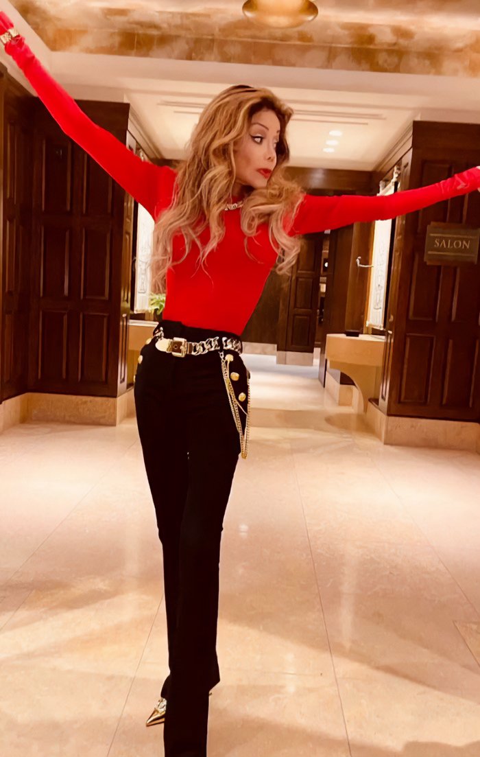 La Toya Jackson in red top and black pants, showing alarmingly slim appearance amid possible health issues indoors.