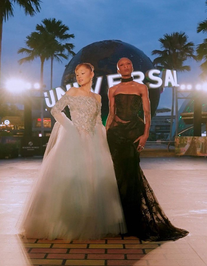 Cynthia Erivo in a striking black gown posing with a woman in a white dress at Universal Studios at dusk.
