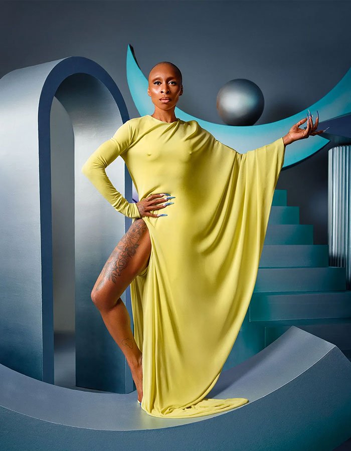 Cynthia Erivo in a flowing yellow gown, posing confidently on a futuristic set, embodying Ariana influence.