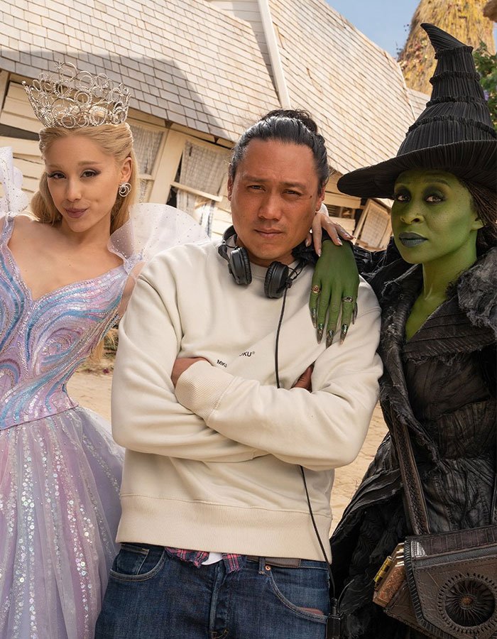 Cynthia Erivo in green witch makeup and a man with headphones between her and a woman in a sparkling princess dress.