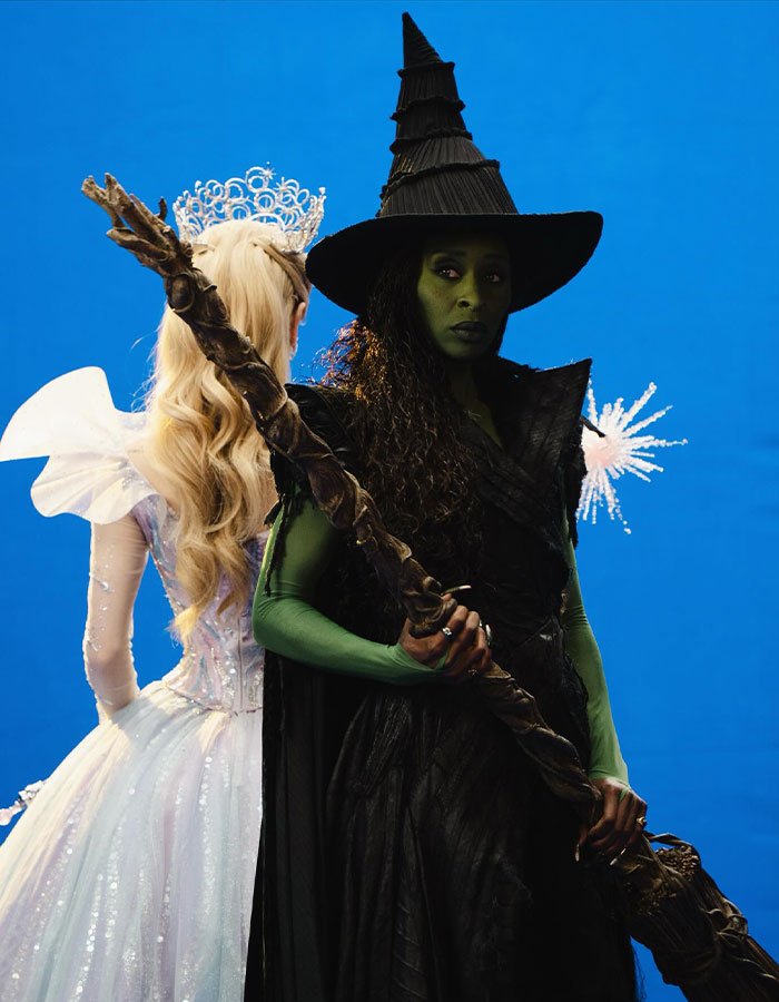 Cynthia Erivo as a green-skinned witch holding a staff, with a fairy-tale princess in a white dress behind her.