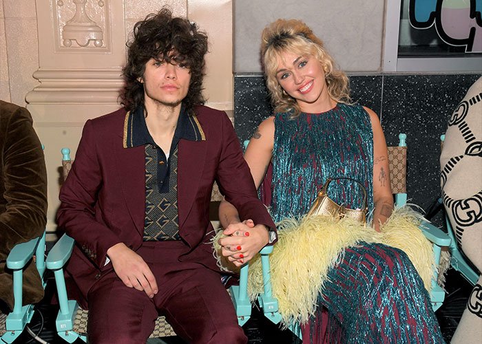 Miley Cyrus and Maxx Morando holding hands, dressed stylishly, sparking engagement and age-related reactions.