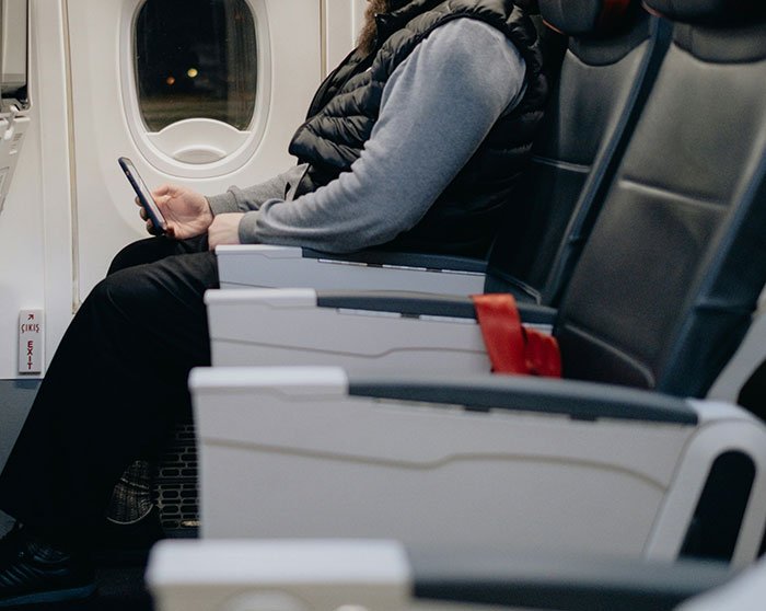Passenger sitting inside airplane cabin looking at phone, highlighting a flight moment connected to body-shaming text incident.