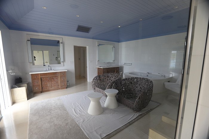 Spacious bathroom inside Epstein’s private island home featuring wicker chairs, twin sinks, and a large bathtub.