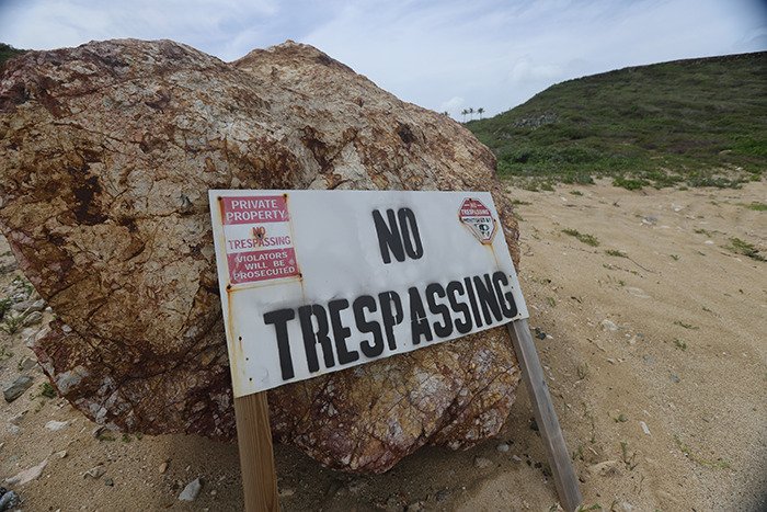 No trespassing sign on sandy ground near large rock at Epstein’s private island home, eerie restricted area view.