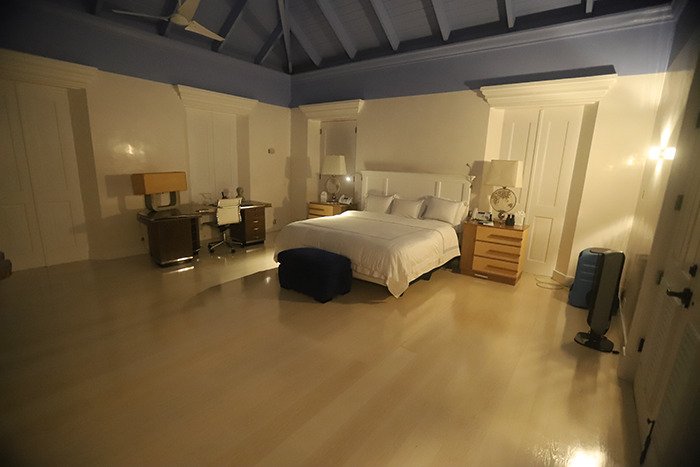 Spacious bedroom inside Epstein’s private island home with a large bed, desk, and soft, dim lighting at night.