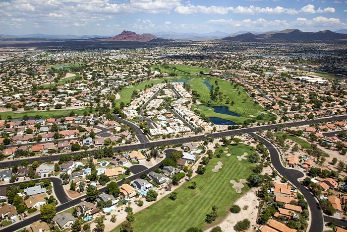 A wide aerial view of a suburban neighborhood with golf courses under a partly cloudy sky.