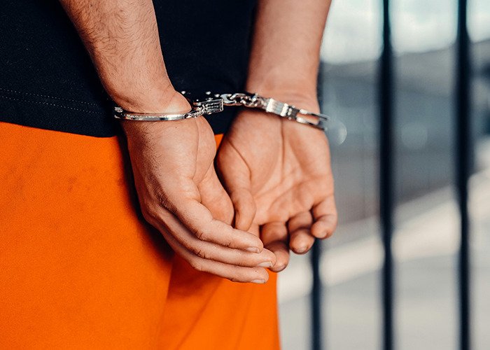 Hands of a person in handcuffs wearing orange pants, symbolizing arrest of a terrible psychopath caught on CCTV footage.