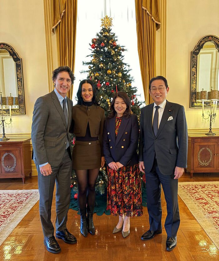 Justin Trudeau and Katy Perry with Japan's ex-PM posing in front of a decorated Christmas tree during a formal meeting.