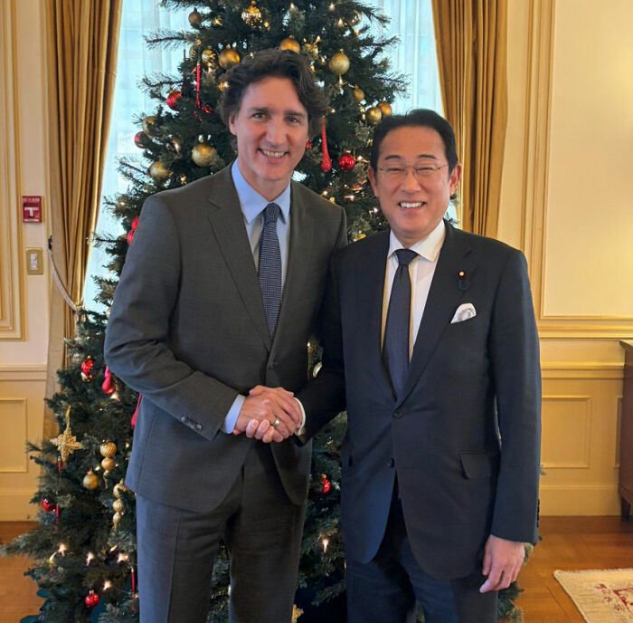 Justin Trudeau and Japan's ex-PM shaking hands in front of a decorated Christmas tree during a formal meeting.