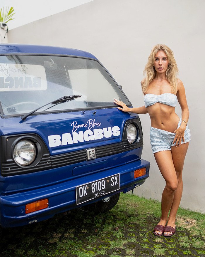 Adult star Bonnie Blue posing next to a blue van labeled Bangbus during a controversial tour outdoors.