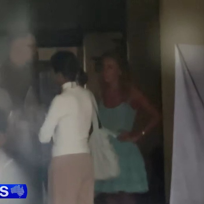 Blurry image of two women indoors, one in a white top and the other in a blue dress, related to adult star Bonnie Blue arrest.