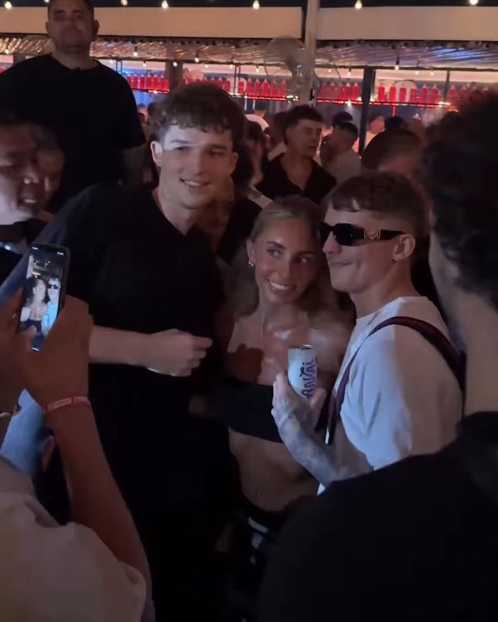 Group of young people smiling and posing for a photo during Bonnie Blue controversial tour event at a crowded venue