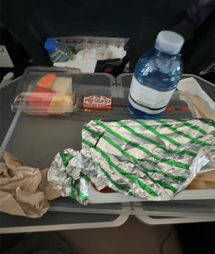 Air Canada passenger meal on tray with water bottle and packaged food items during flight service complaint.