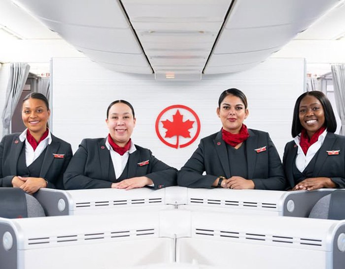 Four Air Canada flight attendants standing inside an airplane cabin with the airline logo visible behind them.
