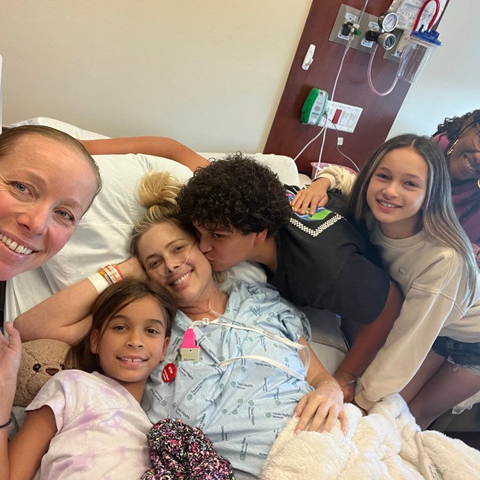 Netflix star and mom of three lying in hospital bed surrounded by family showing love and support in emotional moment