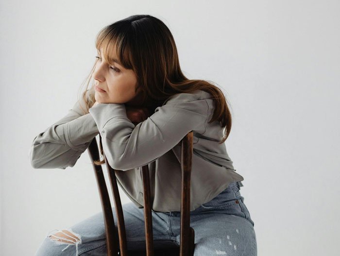 Young woman sitting on a chair looking thoughtful, reflecting on grandparents combining birthday and Christmas gift feelings.