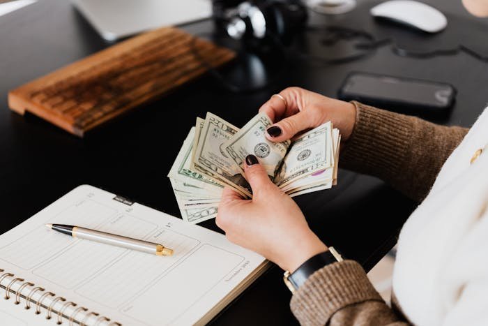 Woman counting cash at desk with planner and pen, illustrating grandparents combine birthday and Christmas gift scenario.