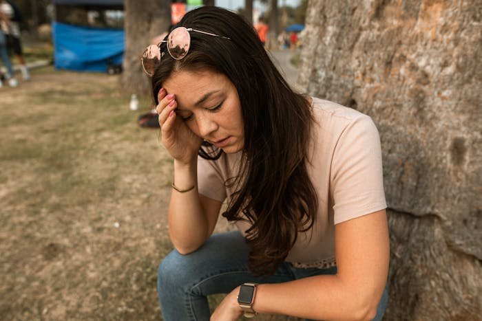 Young woman sitting outdoors looking stressed, representing a mom feeling scammed by grandparents combining birthday and Christmas gifts