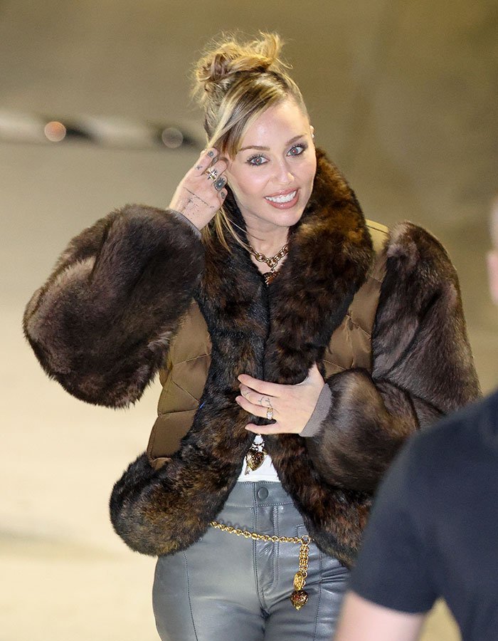 Miley Cyrus smiling with youthful glow, wearing a fur jacket and stylish accessories during her viral makeover moment.