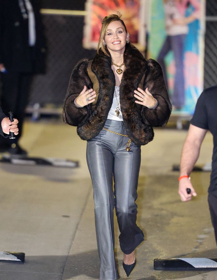 Miley Cyrus smiling and walking outdoors wearing a fur jacket and leather pants showcasing her youthful glow and viral makeover.