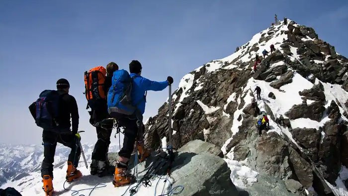 Three climbers in winter gear ascending Austria’s highest peak with snow and rocky terrain under clear blue sky.