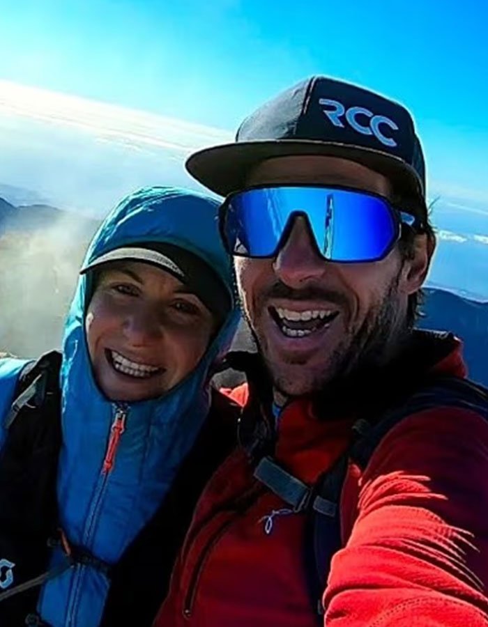 Couple in outdoor gear smiling during a mountain hike, related to woman abandoned to fatally freeze on Austria’s highest peak.