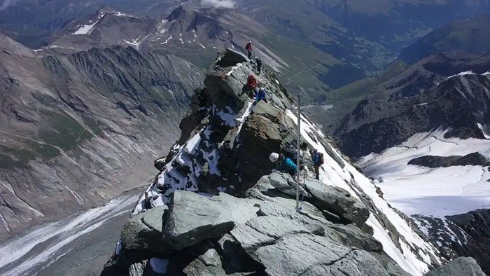Climbers ascending Austria’s highest peak with rocky terrain and snowy patches in a remote mountainous landscape.