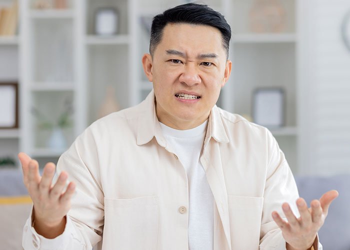 Angry man demanding cousin pay for his cruel prank, expressing frustration in a bright living room setting.