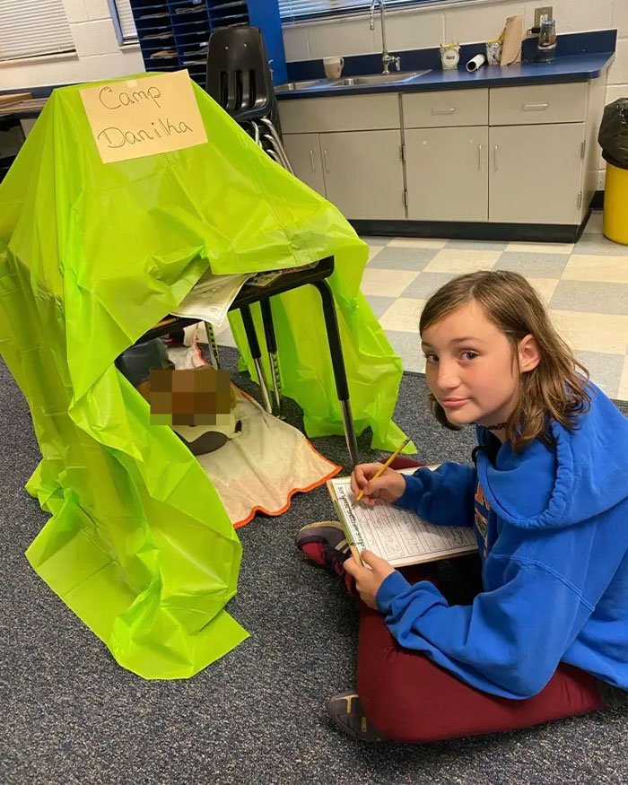 Teen girl sitting on floor next to a small green tent labeled Camp Danika in a classroom setting.
