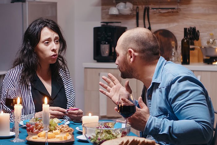 Couple having tense conversation at dinner, highlighting his girlfriend wanting him to close her closet door.